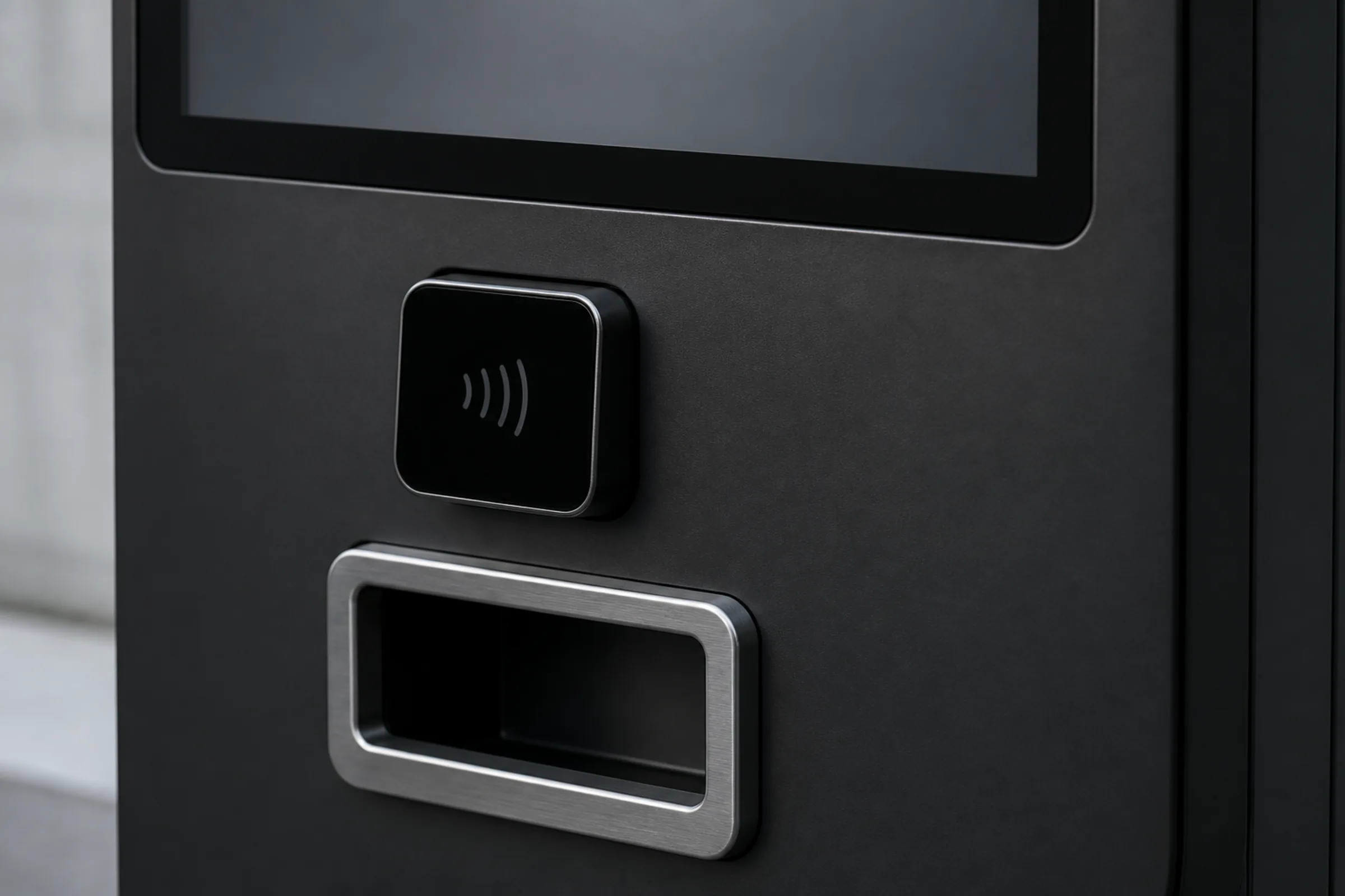 Close-up of a contactless card reader and the stainless dispensing bin on a matte black kiosk fascia, with the lower edge of the touchscreen above.